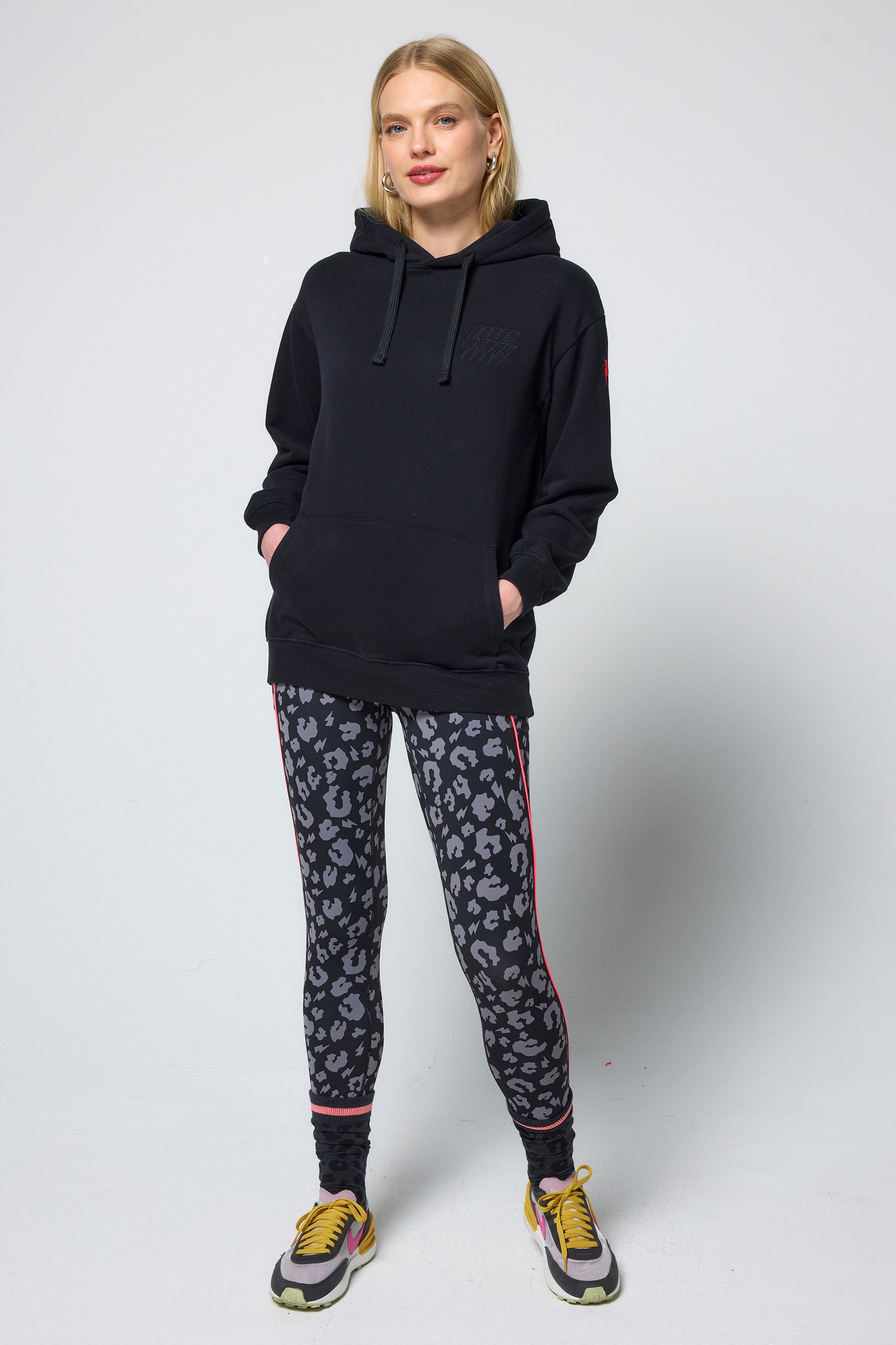 Scamp & Dude Black Multi Neon Bolt Longline Hoodie | Model wearing a black hoodie and patterned leggings on a white background.