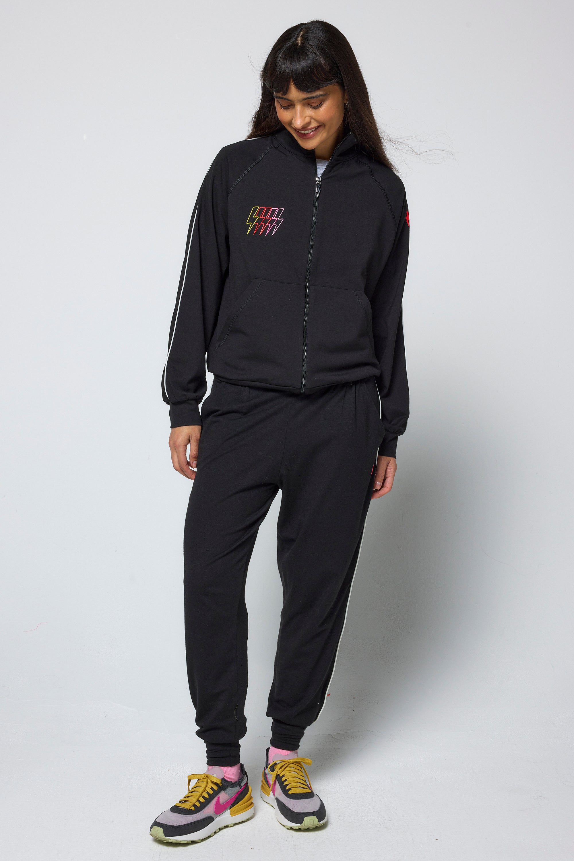 Scamp and Dude Black Funnel Neck Zip Through Top | Model wearing a black funnel neck zip through top with matching joggers and colourful trainers.