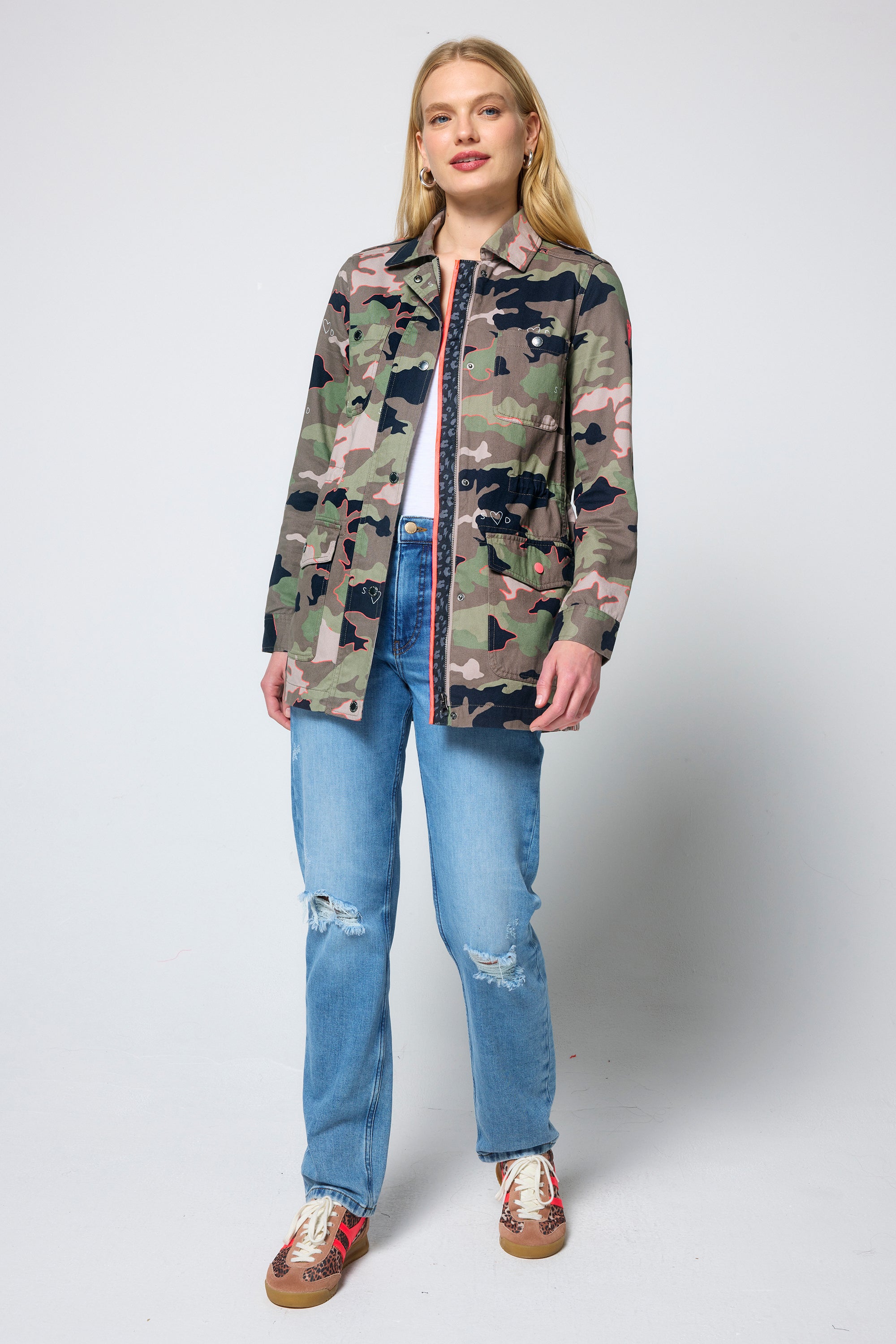 Scamp & Dude Khaki Camo Utility Jacket | Model wearing a khaki camo print utility jacket with distressed blue jeans and neutral cheetah print trainers.