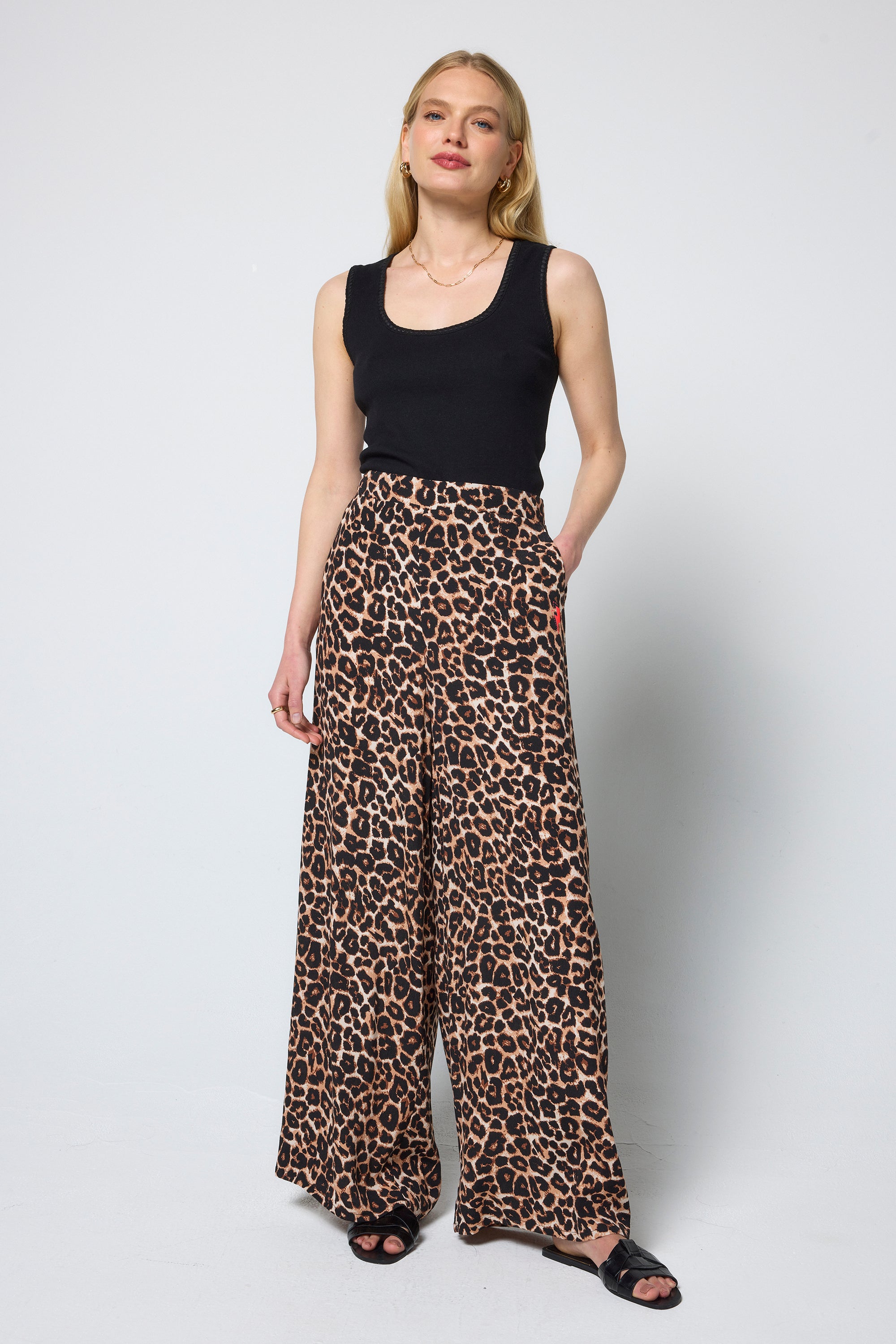 Scamp & Dude Neutral Jaguar Wide Leg Trousers | Model wearing a black tank top and jaguar print wide leg trousers on a white background.