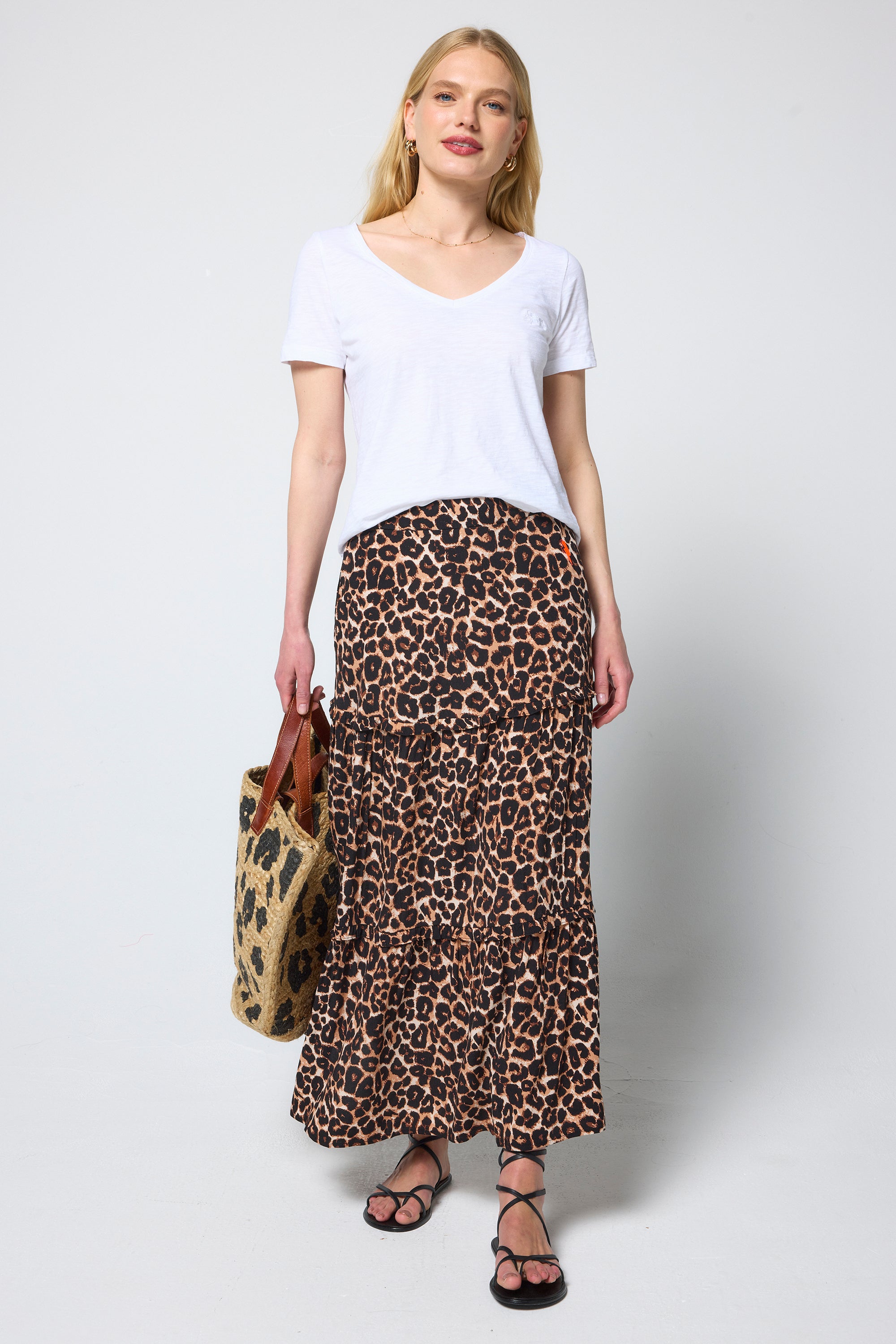 Scamp and Dude Neutral Jaguar Tiered Midi Skirt | Model wearing a neutral jaguar midi skirt with a white v-neck t-shirt and straw bag.