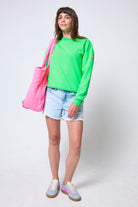 Scamp & Dude Neon Green Washed Ultimate Sweatshirt | Model wearing a bright green sweatshirt, denim shorts, and blue trainers, holding a pink bag.