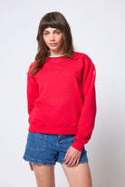 Scamp & Dude Red Embroidered Logo Ultimate Sweatshirt | Model wearing a red sweatshirt and denim shorts with cheetah print Gola trainers.