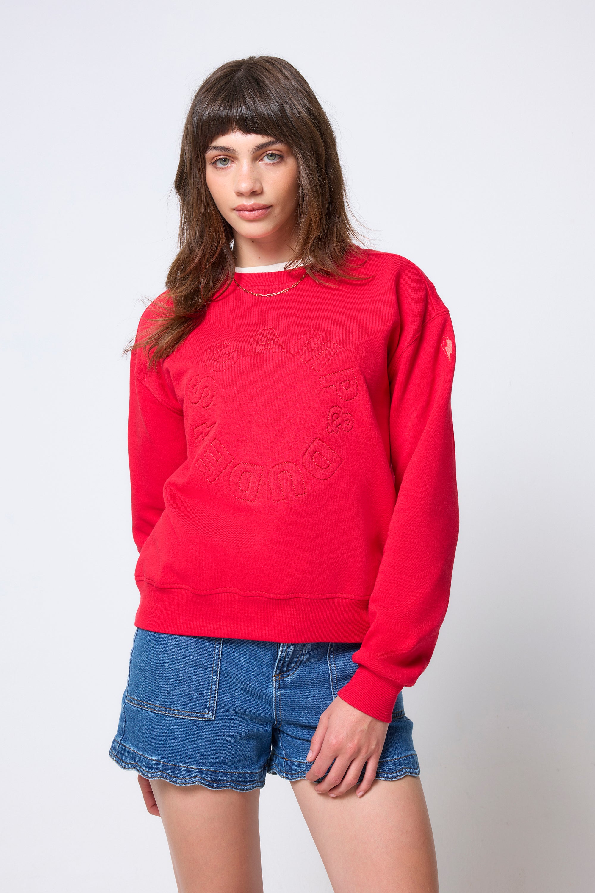 Scamp & Dude Red Embroidered Logo Ultimate Sweatshirt | Model wearing a red sweatshirt and denim shorts with cheetah print Gola trainers.