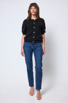 Scamp & Dude Black Short Sleeve Cardigan | Model wearing a black short sleeve cardigan with gold heart button detail. Worn with blue boyfriend jeans and heels.