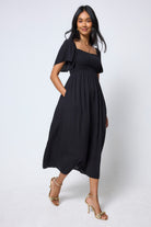 Scamp & Dude Black Shirred Square Neck Midi Dress | Model wearing a black dress square neck dress with gold high heels.