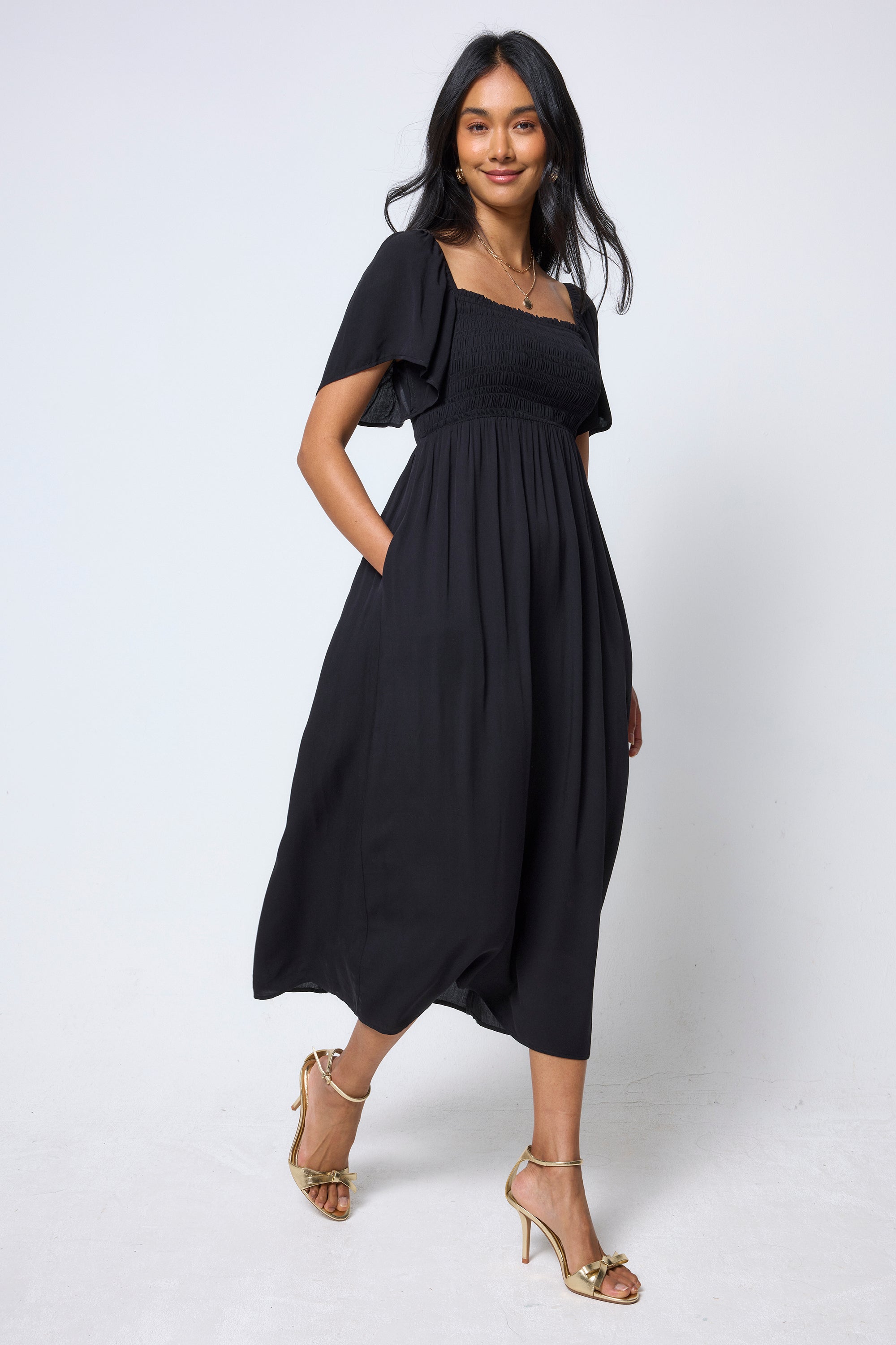Scamp & Dude Black Shirred Square Neck Midi Dress | Model wearing a black dress square neck dress with gold high heels.