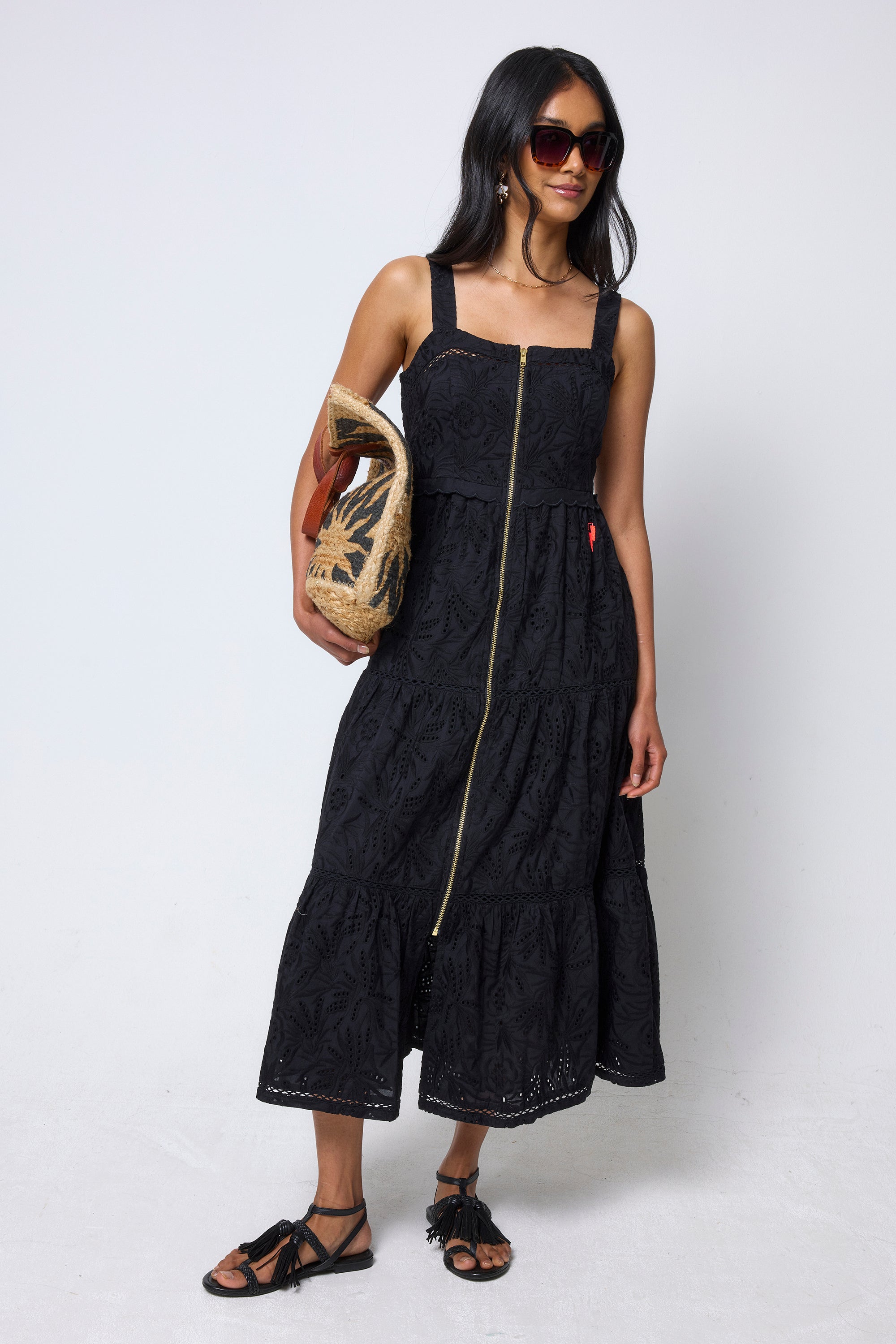 Scamp & Dude Black Broderie Zip Detail Midi Sundress | Model wearing a black dress with a zipper, holding a woven bag on a white background.