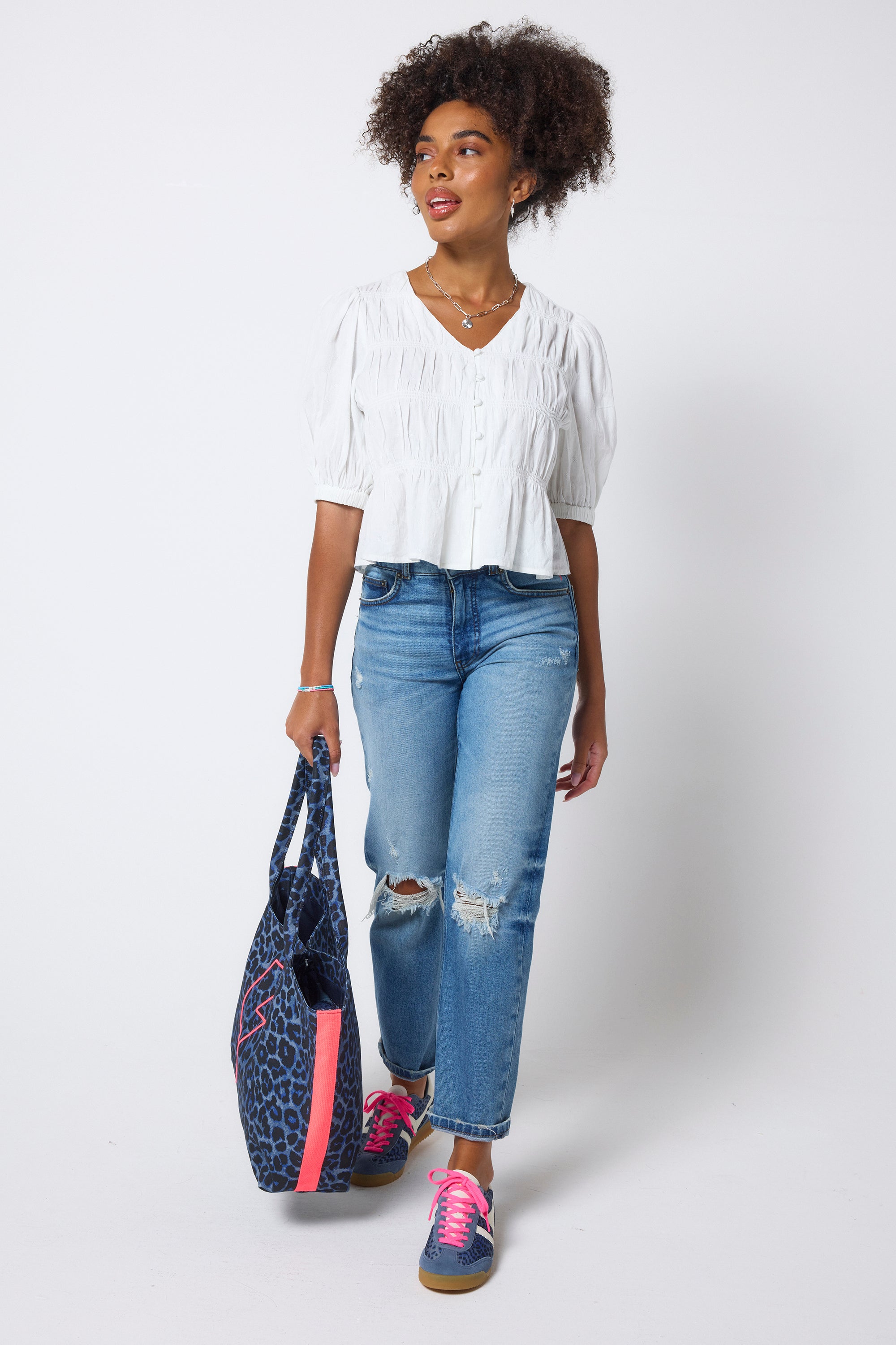 Scamp & Dude White Puff Sleeve Smocked Blouse | Model wears a short sleeve smocked blouse with distressed blue jeans and trainers.