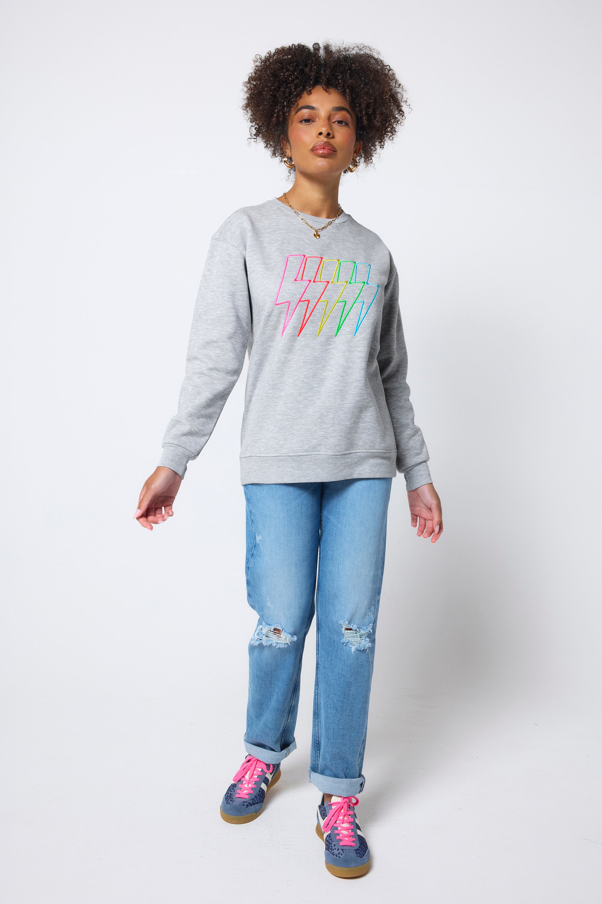 Scamp & Dude Grey Marl Multi Neon Bolt Longline Sweatshirt | Model wearing a grey longline sweatshirt with neon bolt detail. Worn with distressed blue jeans and blue trainers.