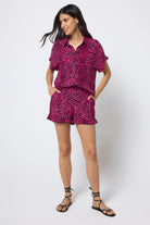 Scamp & Dude Pink with Black Wild Leopard Frill Hem Shorts | Model wearing pink leopard print shorts with frill detail and a matching shirt. Worn with black flat sandals.