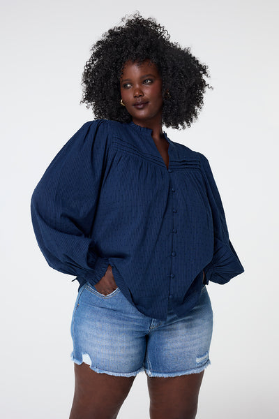 Scamp and Dude Navy Dobby Frill Neck Blouse | Model wearing long sleeve blouse featuring puff sleeves with frill neck and dobby detail.