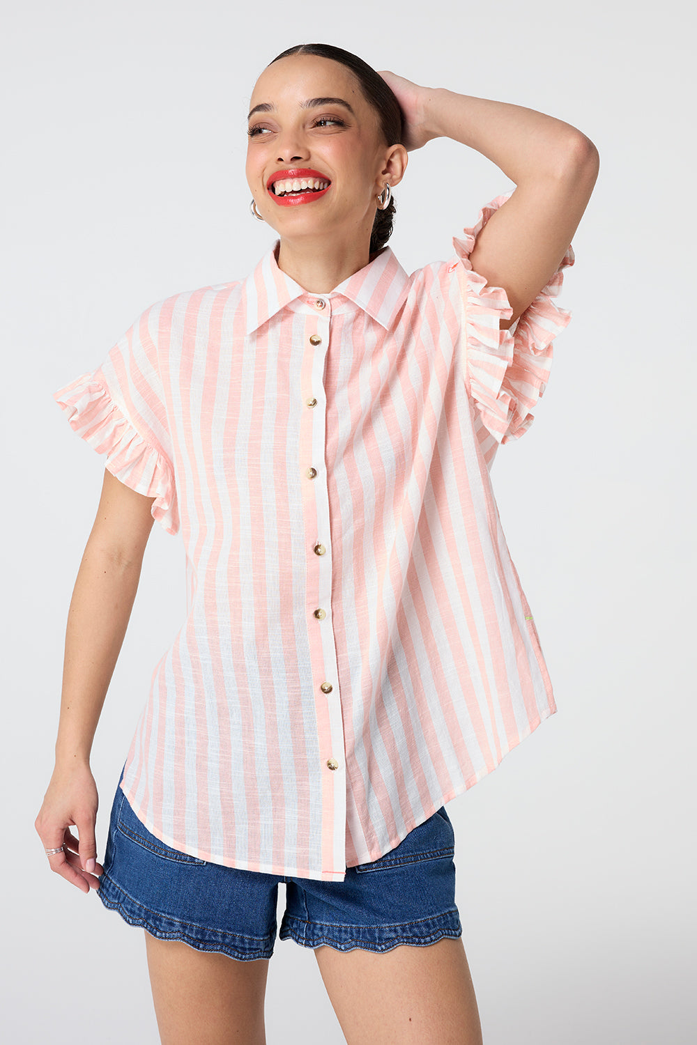 Scamp and Dude Coral and White Stripe Frill Sleeve Shirt | Model wearing coral and white stripe shirt featuring frill sleeves and paired with scallop hem denim shorts.