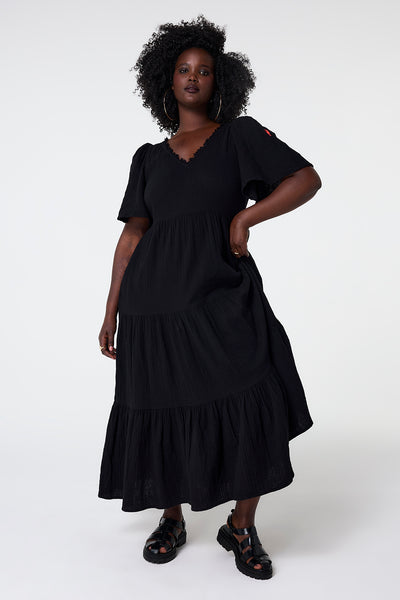 Scamp and Dude Black Flute Sleeve Tiered Midi Dress | Model wearing black midi dress with v neckline, flute sleeve and tiered skirt detail.