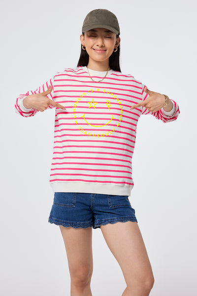 Scamp and Dude Ivory with Neon Pink Stripe and Smiley Face Oversized Sweatshirt | Model wearing a round neck sweatshirt featuring stripes and smiley face, worn with scallop hem denim shorts and a khaki cap.