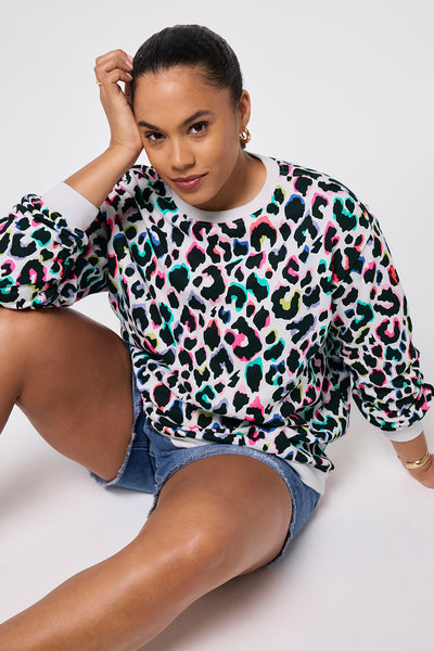 Scamp and Dude Ivory with Rainbow Shadow Leopard Oversized Sweatshirt | Model wearing an ivory oversized sweatshirt with rainbow shadow leopard print, paired with blue denim shorts and gold jewellery.