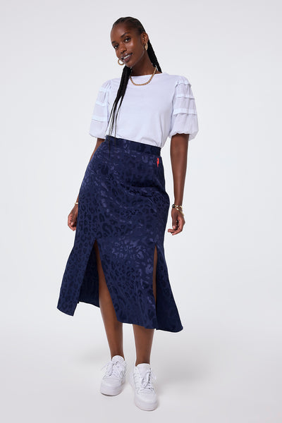 Scamp and Dude Navy Jacquard Leopard Split Front Skirt | Model wearing navy split front midi skirt with jacquard leopard detail, paired with a white pintuck sleeve t shirt and trainers.