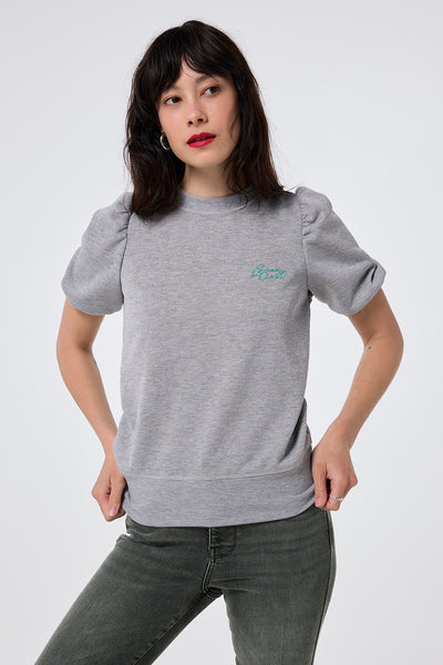 Scamp and Dude Grey Lurex Puff Sleeve Sweatshirt | Model wearing grey lurex sweatshirt with short puff sleeves and turquoise embroidered logo paired with washed black jeans.