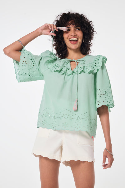 Scamp and Dude Green Cutwork Blouse | Model wearing green cutwork blouse featuring tie front detail with tassels. Worn with ecru denim shorts and sandals.
