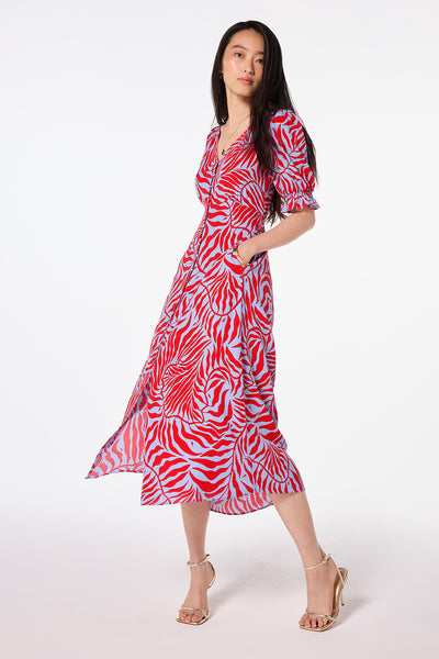Scamp and Dude Blue with Red Palm Flute Sleeve Midi Tea Dress | Model wearing a red midi tea dress with blue palm print paired with gold strappy heels.