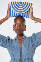 Scamp and Dude Natural with Blue Stripe Straw Clutch Bag | Model wearing blue denim midi dress with a natural and blue stripe straw clutch bag.