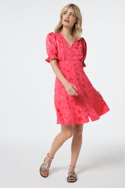 Scamp and Dude Coral Star Jacquard Flute Sleeve Short Tea Dress | Model wearing a coral flute sleeve short tea dress in a star jacquard finish, paired with studded sandals.
