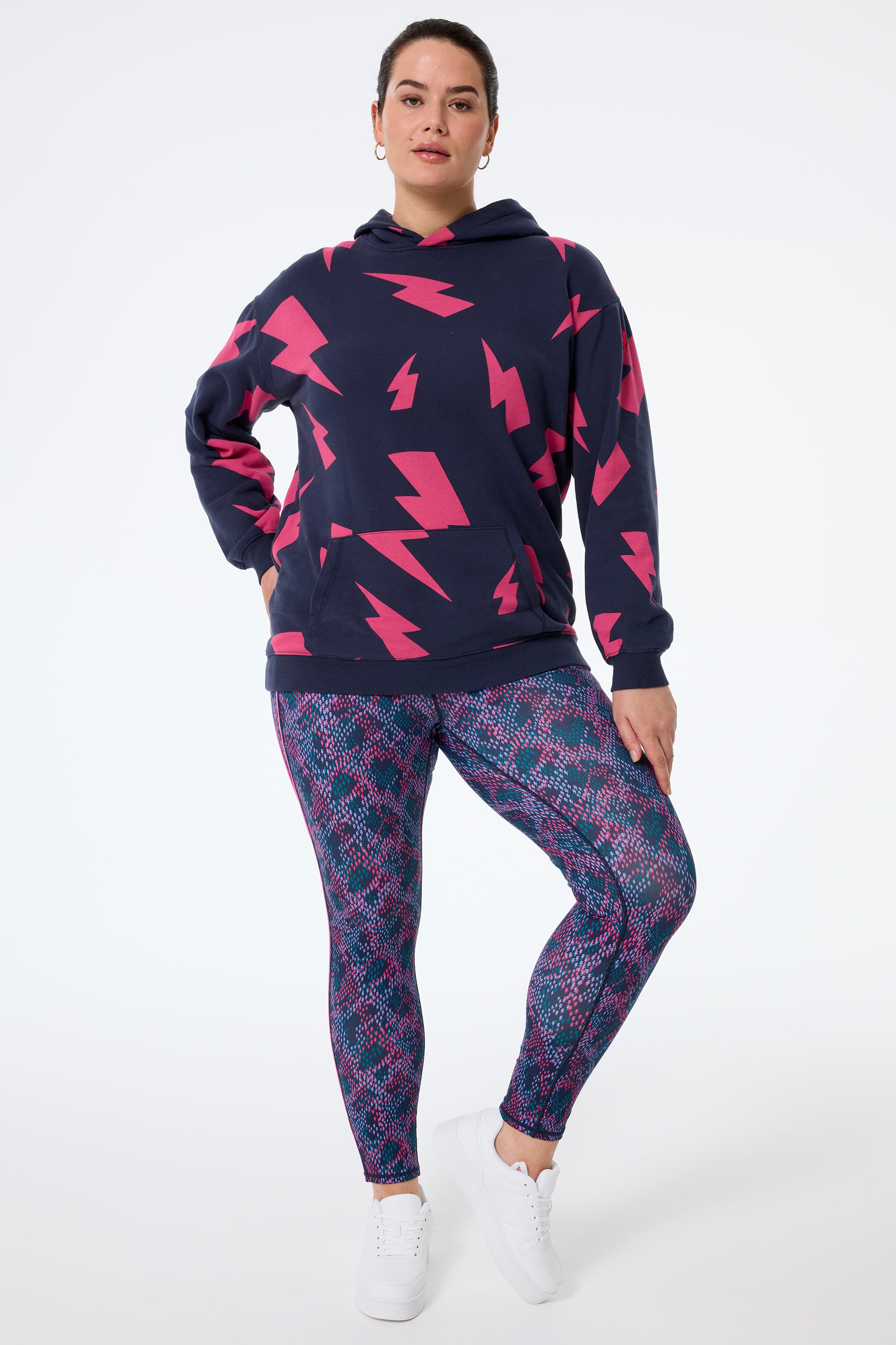 Scamp and Dude Navy with Pink Mega Lightning Bolt Longline Hoodie | Model wearing navy hoodie featuring pink mega lightning bolts paired with snake bolt print leggings and white trainers.