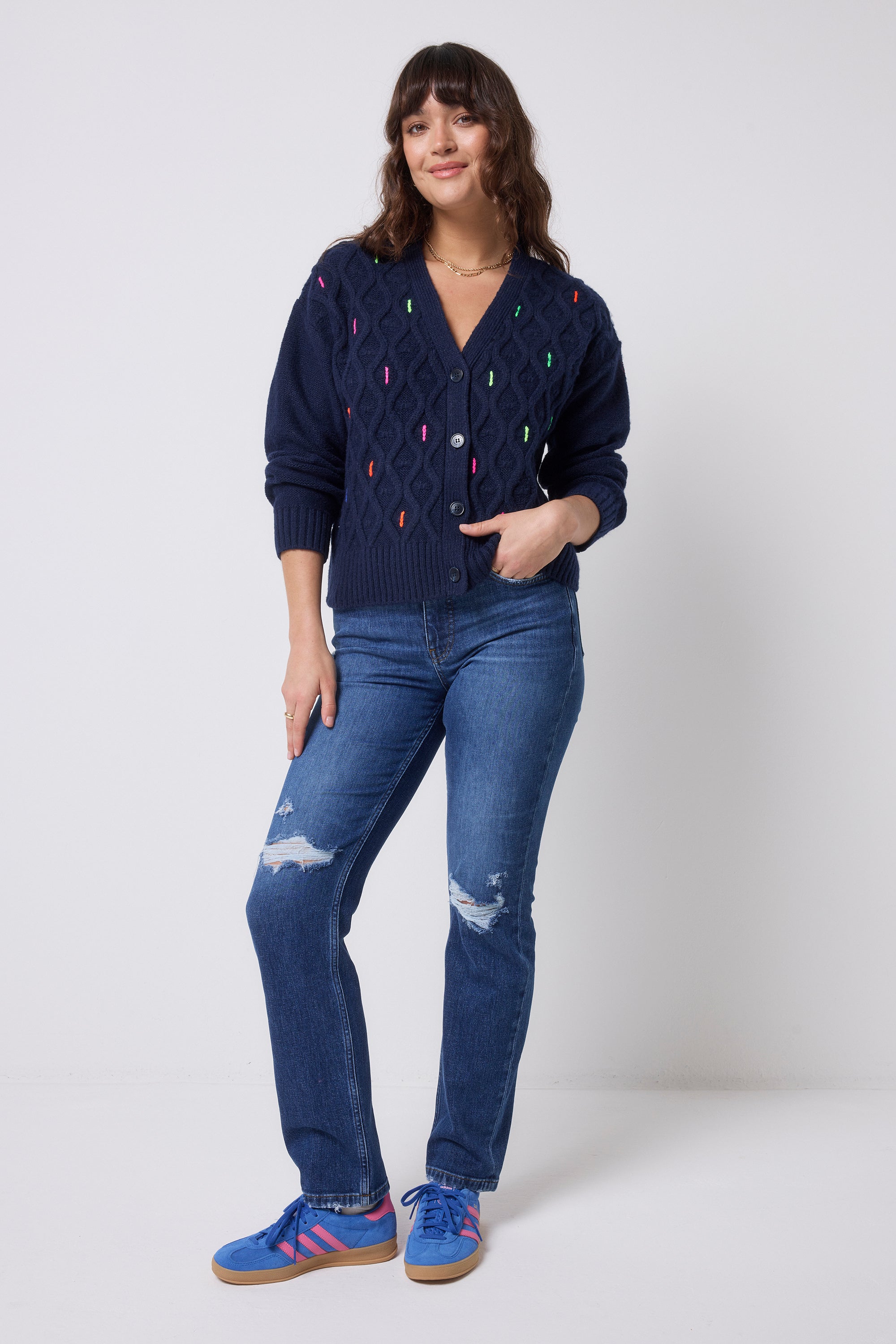 Scamp & Dude Navy with Neon Rainbow Flecks Cable Knit Cardigan | Model wearing a navy cardigan with colourful neon flecks and blue jeans.