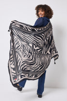 Scamp & Dude Black and White Zebra and Lightning Bolt Charity Super Scarf | Model wearing a blue denim blouse and jeans with a large black and white patterned scarf.
