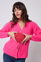 Scamp and Dude Red Heart Purse | Model wearing a neon pink cardigan with dark blue jeans holding a red heart shaped purse.