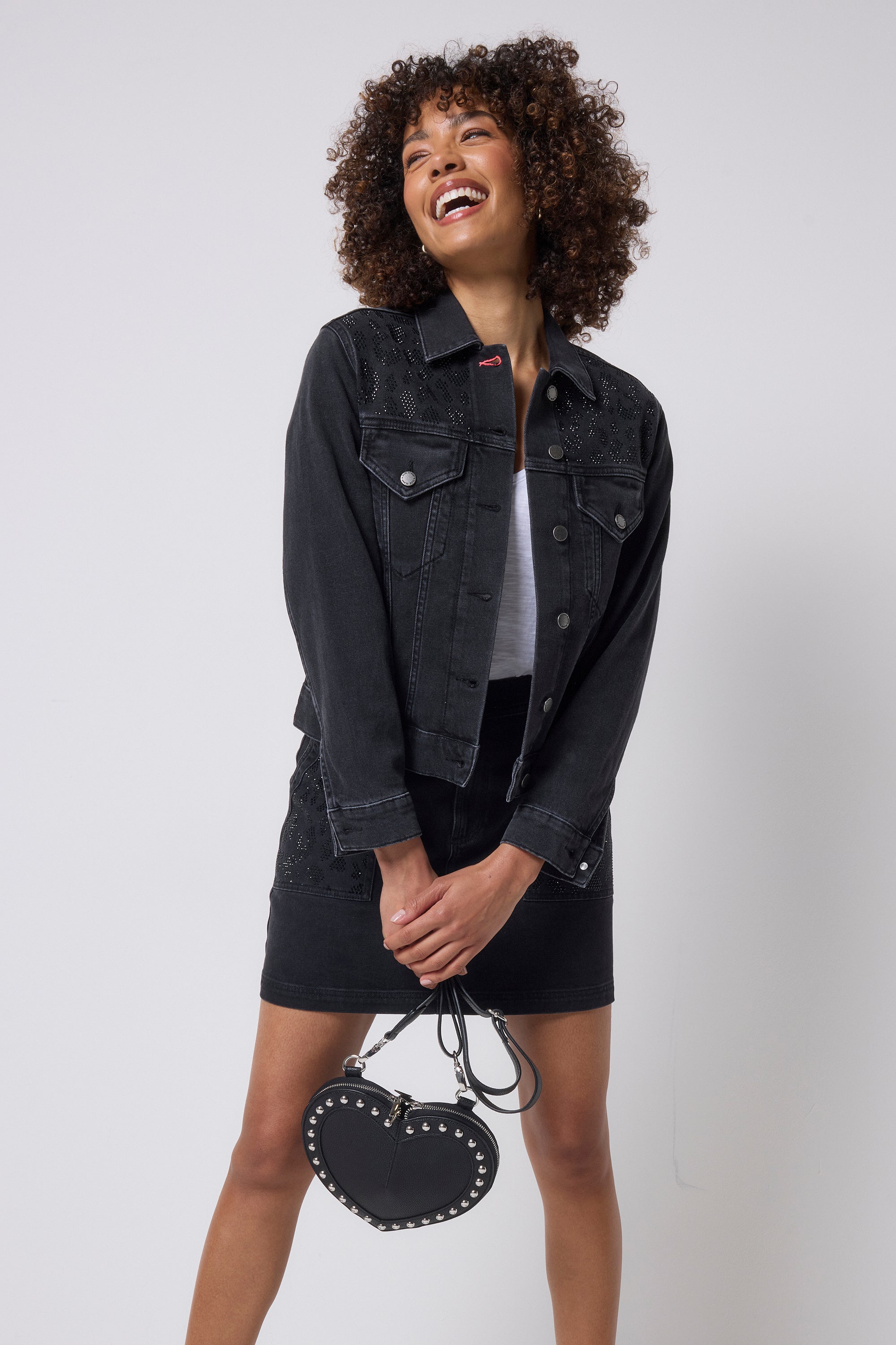 Scamp & Dude Washed Black Embellished Leopard Denim Jacket | Model wearing a black denim jacket and mini skirt with embellished detail holding a heart shaped bag.
