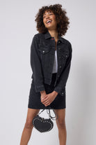 Scamp & Dude Washed Black Embellished Leopard Denim Jacket | Model wearing a black denim jacket and mini skirt with embellished detail holding a heart shaped bag.