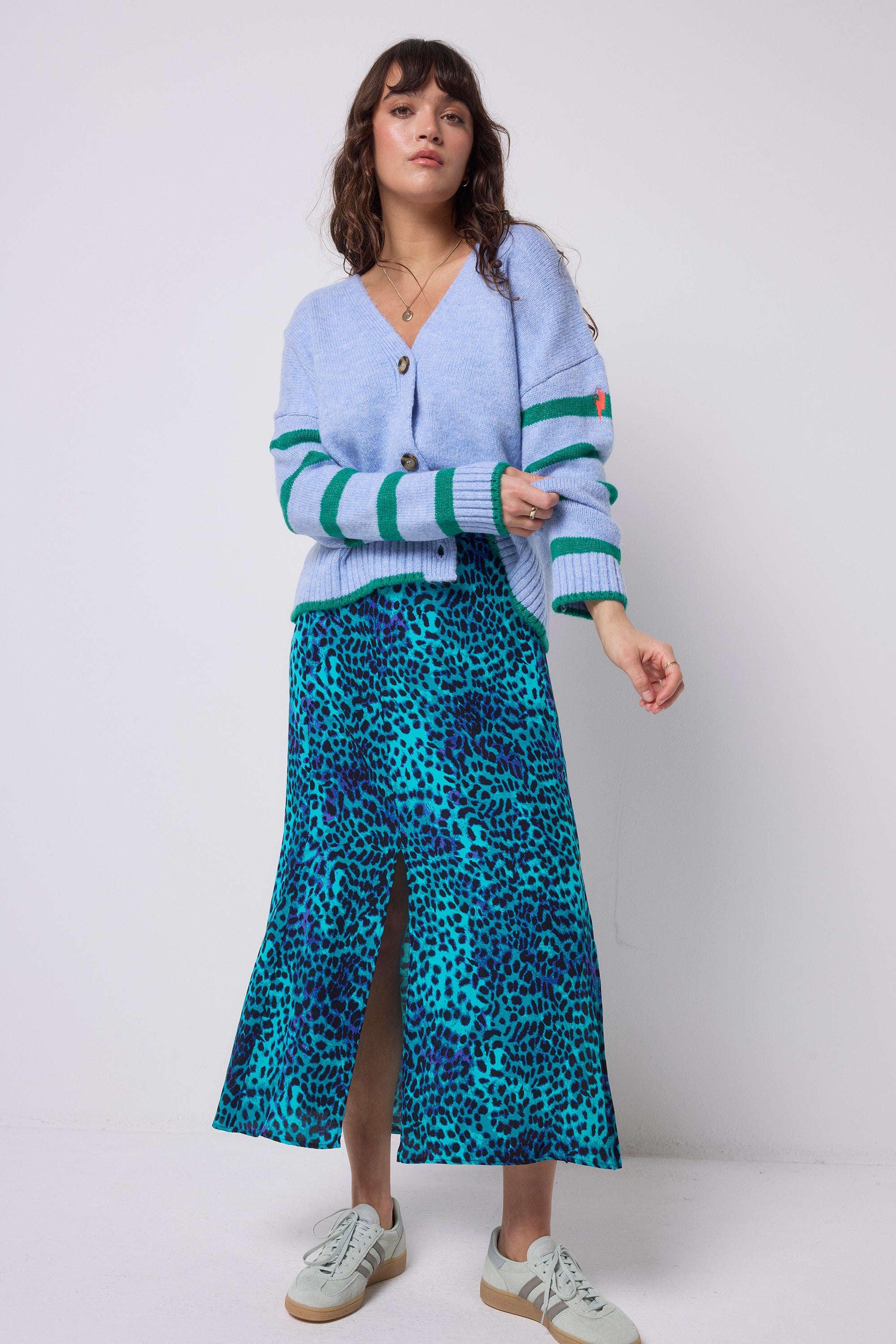 Scamp & Dude Turquoise with Blue Cheetah Split Front Skirt | Model wearing a light blue cardigan with green stripes and a turquoise cheetah print skirt with trainers.