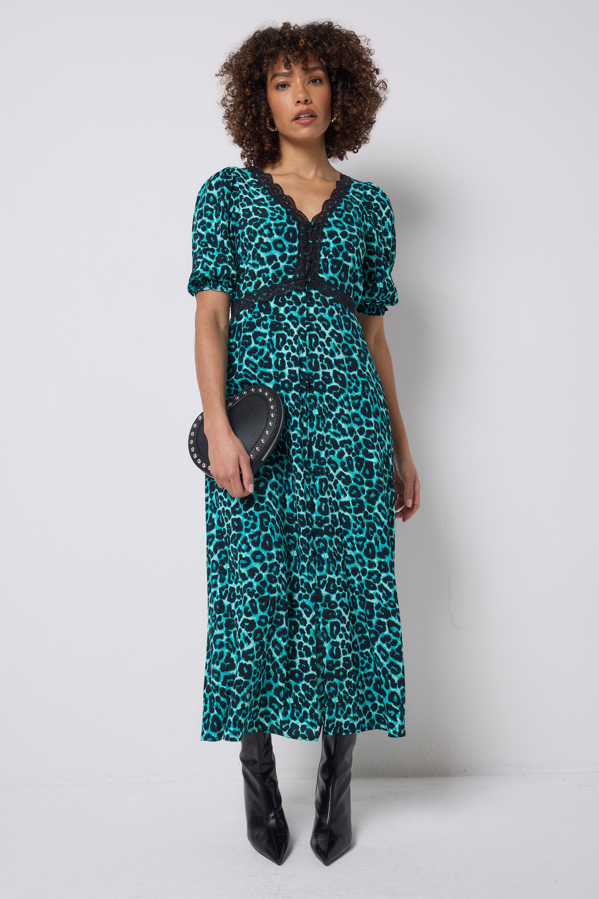 Scamp and Dude Green Jaguar Lace Trim Puff Sleeve Midi Tea Dress | Model wearing a green jaguar print midi dress with lace trim detail. Paired with black heeled boots and a black heart shaped bag.