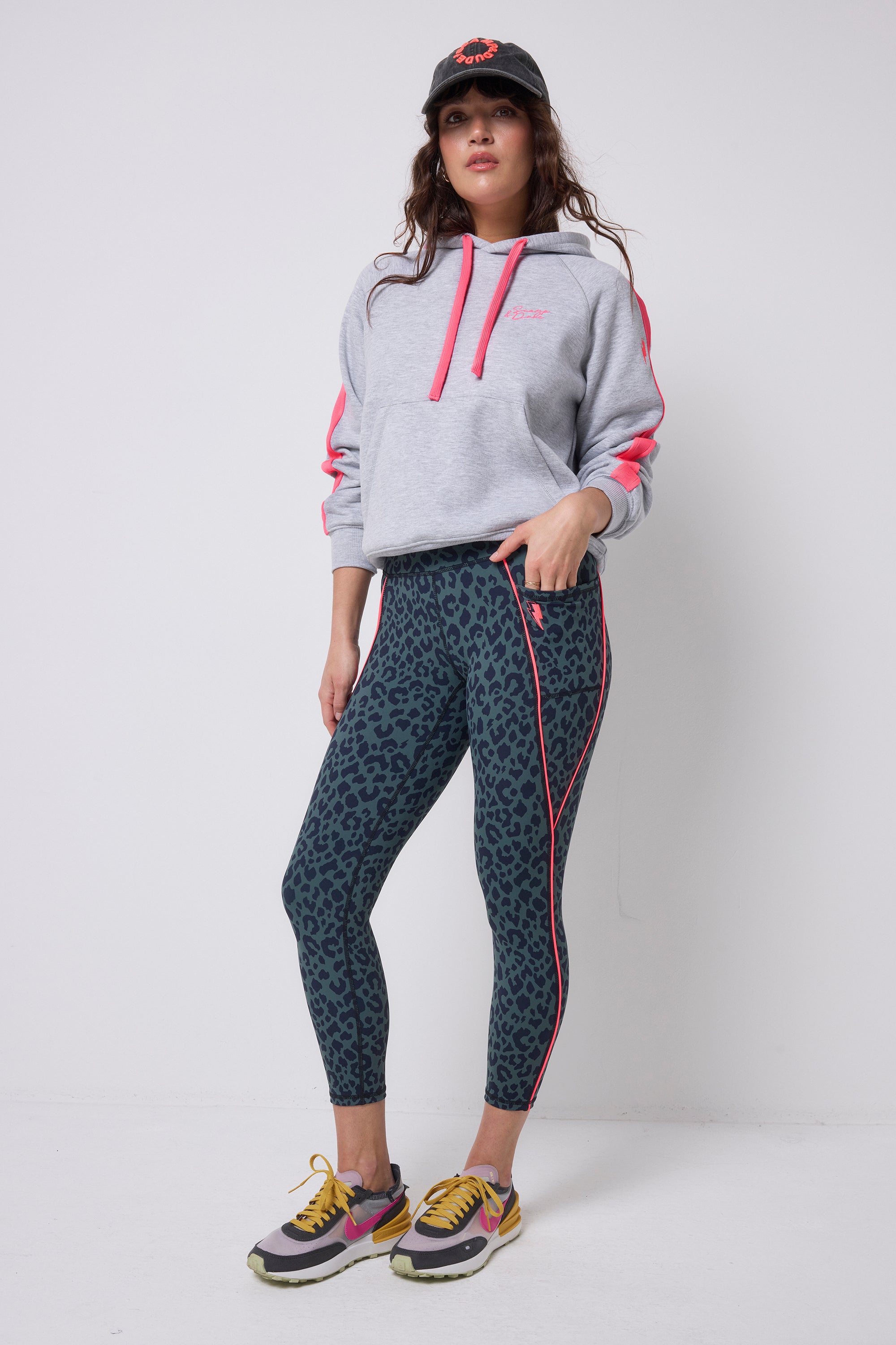 Scamp & Dude Khaki with Navy Candy Leopard 7/8 Length Active Leggings | Model wearing a grey hoodie with a pair of khaki leopard print leggings and colourful chunky trainers.