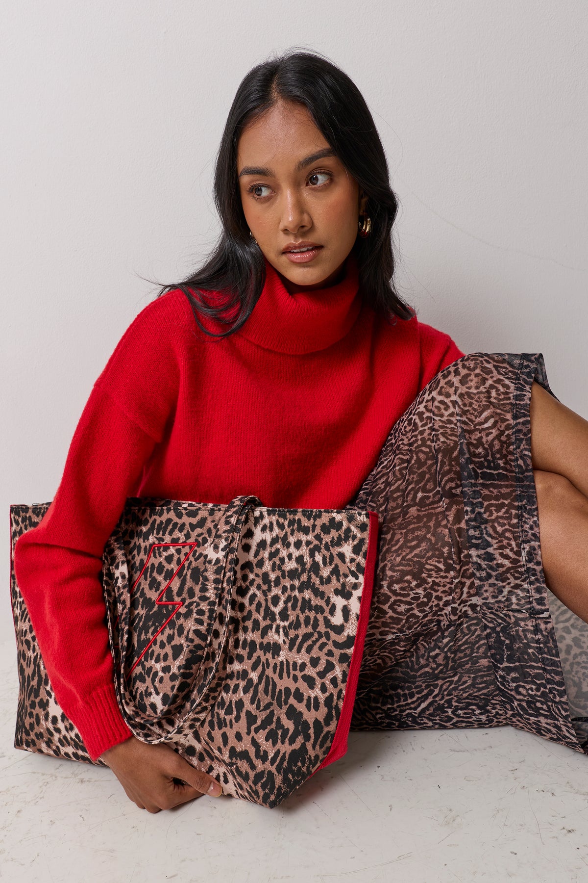Scamp & Dude Neutral Milano Leopard Canvas Shopper Bag | Model wearing a red roll neck jumper with a neutral cheetah skirt and a matching shopper tote bag with a red embroidered bolt.