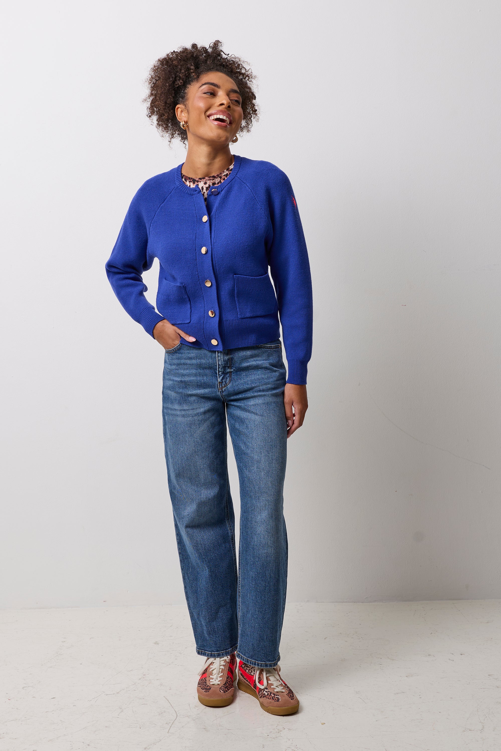Scamp & Dude Cobalt Blue Knitted Bomber | Model wearing a blue knitted bomber with gold buttons. Paired with blue jeans and neutral cheetah gola trainers.