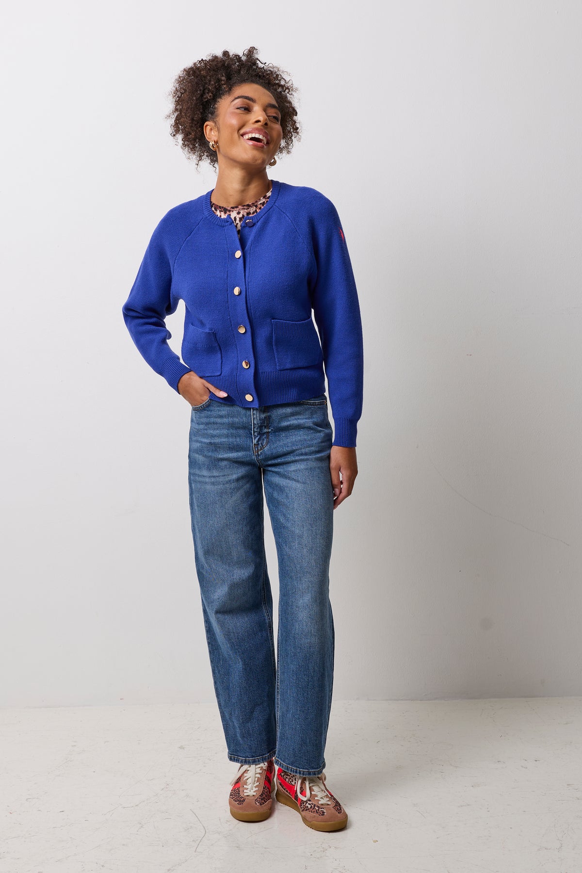 Scamp & Dude Cobalt Blue Knitted Bomber | Model wearing a blue knitted bomber with gold buttons. Paired with blue jeans and neutral cheetah gola trainers.