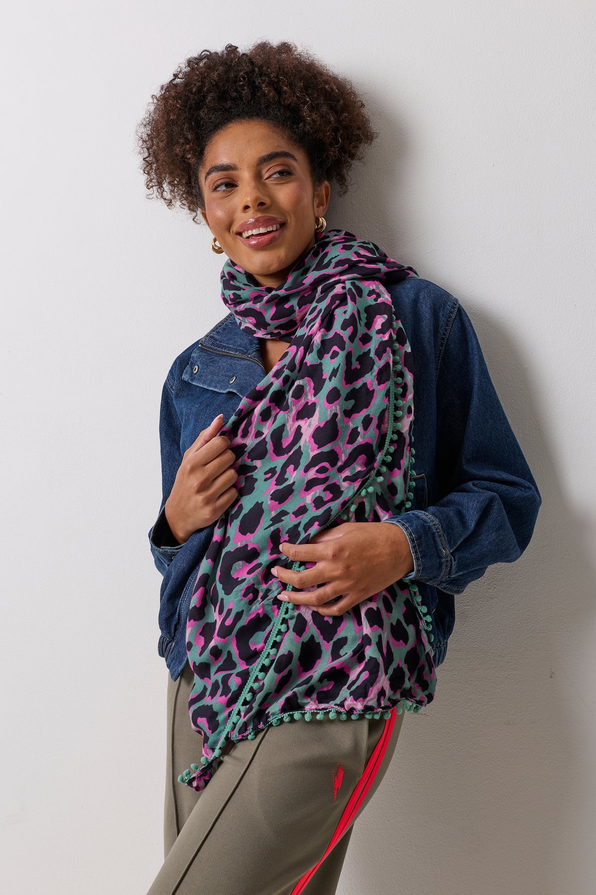 Scamp & Dude Khaki with Pink and Black Shadow Leopard Charity Super Scarf | Model wearing a pair of khaki wide leg trousers, a denim bomber jacket with a funnel neck and a khaki and pink leopard print super scarves.