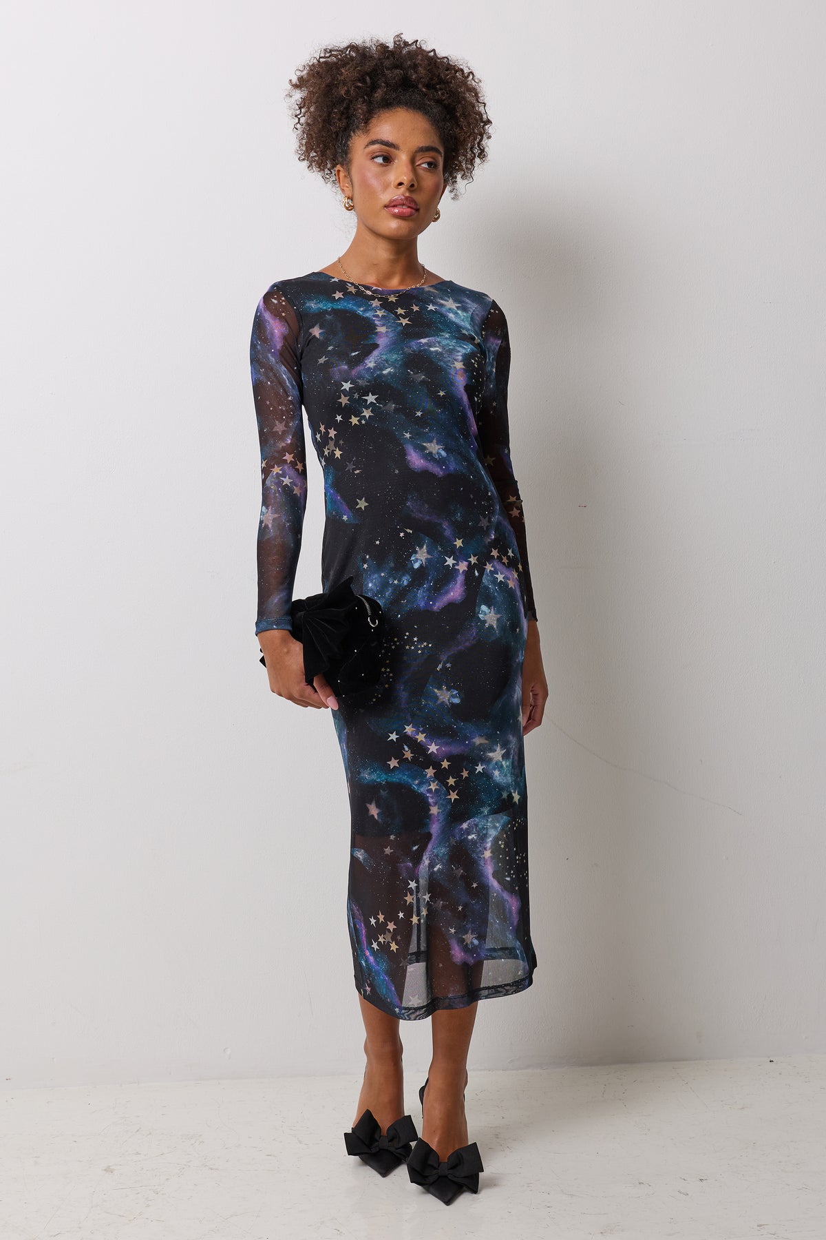 Scamp & Dude Black Galaxy Mesh Midi Dress | Model wearing a black galaxy print mesh midi dress with black bow heels and a matching bag.