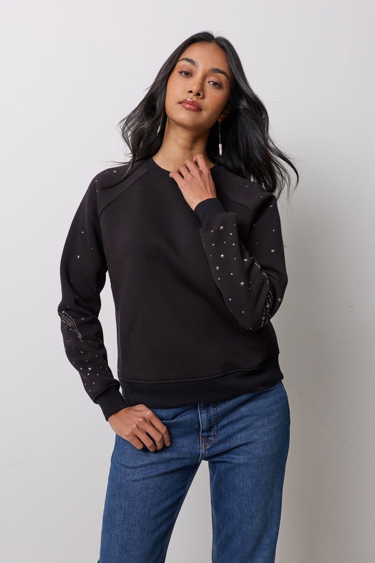 Scamp & Dude Black Written In The Stars Studded Sweatshirt | Model is wearing a black sweatshirt with the star stud detail and blue jeans.