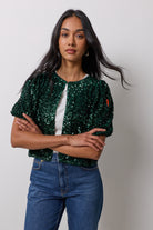Scamp & Dude Green Velvet Sequin Top | Model wearing a green sequin top with a hook and eye front closure over a white t-shirt. Worn with blue jeans.