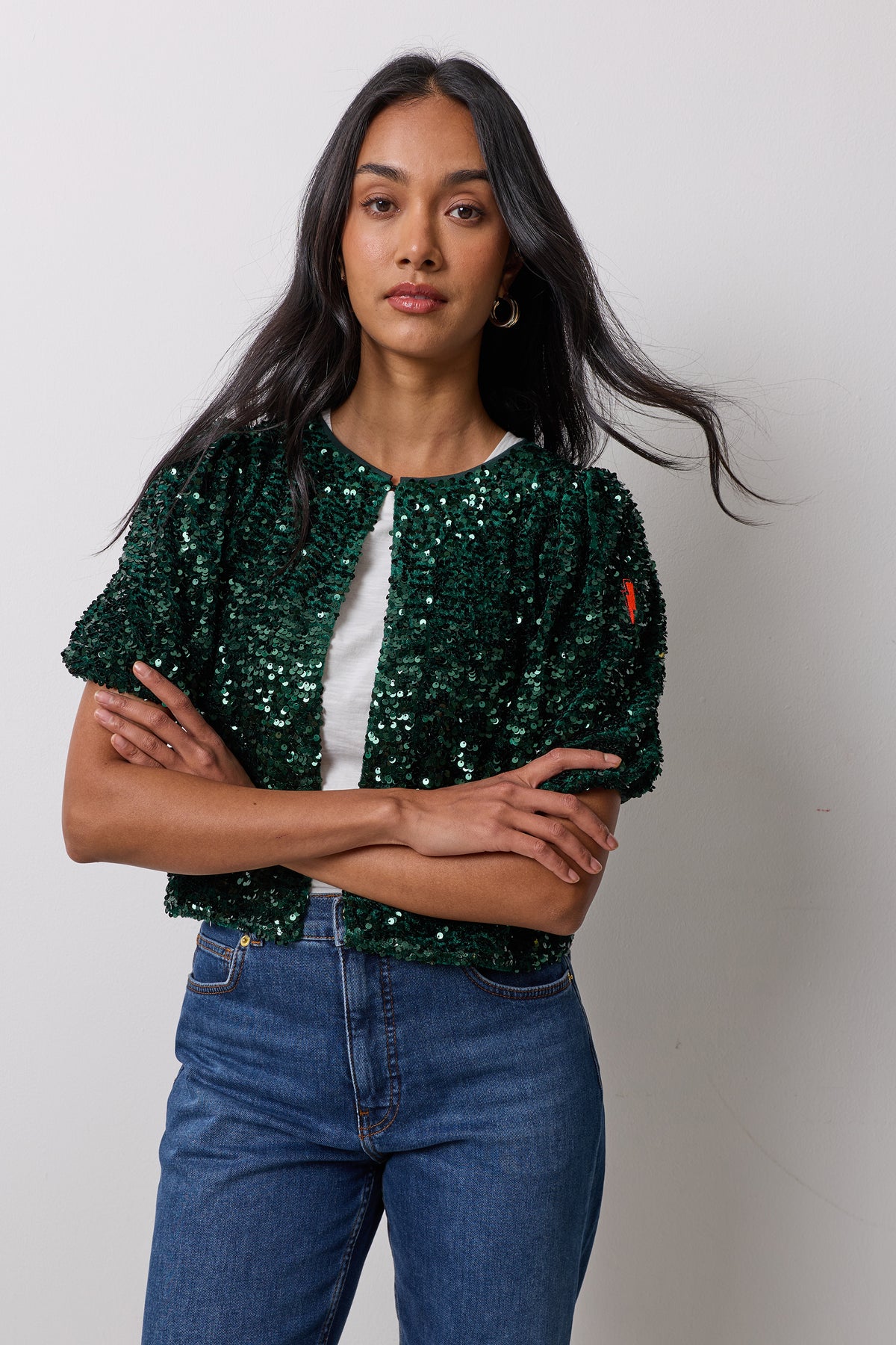 Scamp & Dude Green Velvet Sequin Top | Model wearing a green sequin top with a hook and eye front closure over a white t-shirt. Worn with blue jeans.