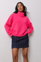 Scamp & Dude Neon Pink Roll Neck Knitted Jumper | Model wearing a bright pink turtleneck knit sweater paired with a dark denim mini skirt.