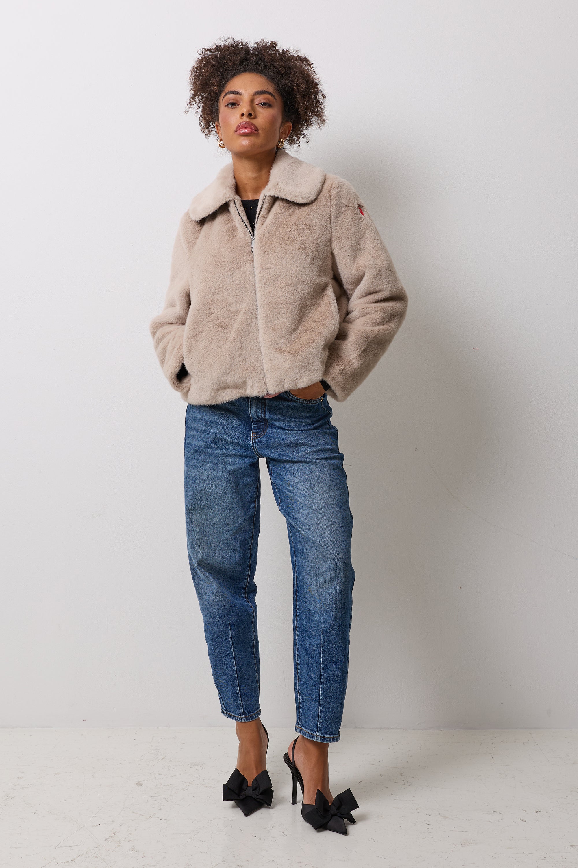 Scamp and Dude Cream Faux Fur Jacket | Model wearing blue jeans with a faux fur jacket and black bow heels.