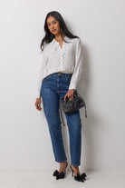 Scamp & Dude White with Black Written In The Stars Shirt | Model wearing a white long-sleeve button-up blouse with small black polka dots, paired with blue jeans, black bow heels, and holding a black studded bucket bag.