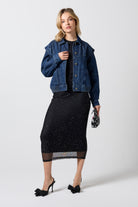 Scamp & Dude Mid Wash Seam Detail Denim Jacket | Model wearing a dark blue denim jacket over a black top, a black midi skirt with subtle silver speckles, and black pointed-toe heels. She is holding a small black-and-white beaded patterned clutch.