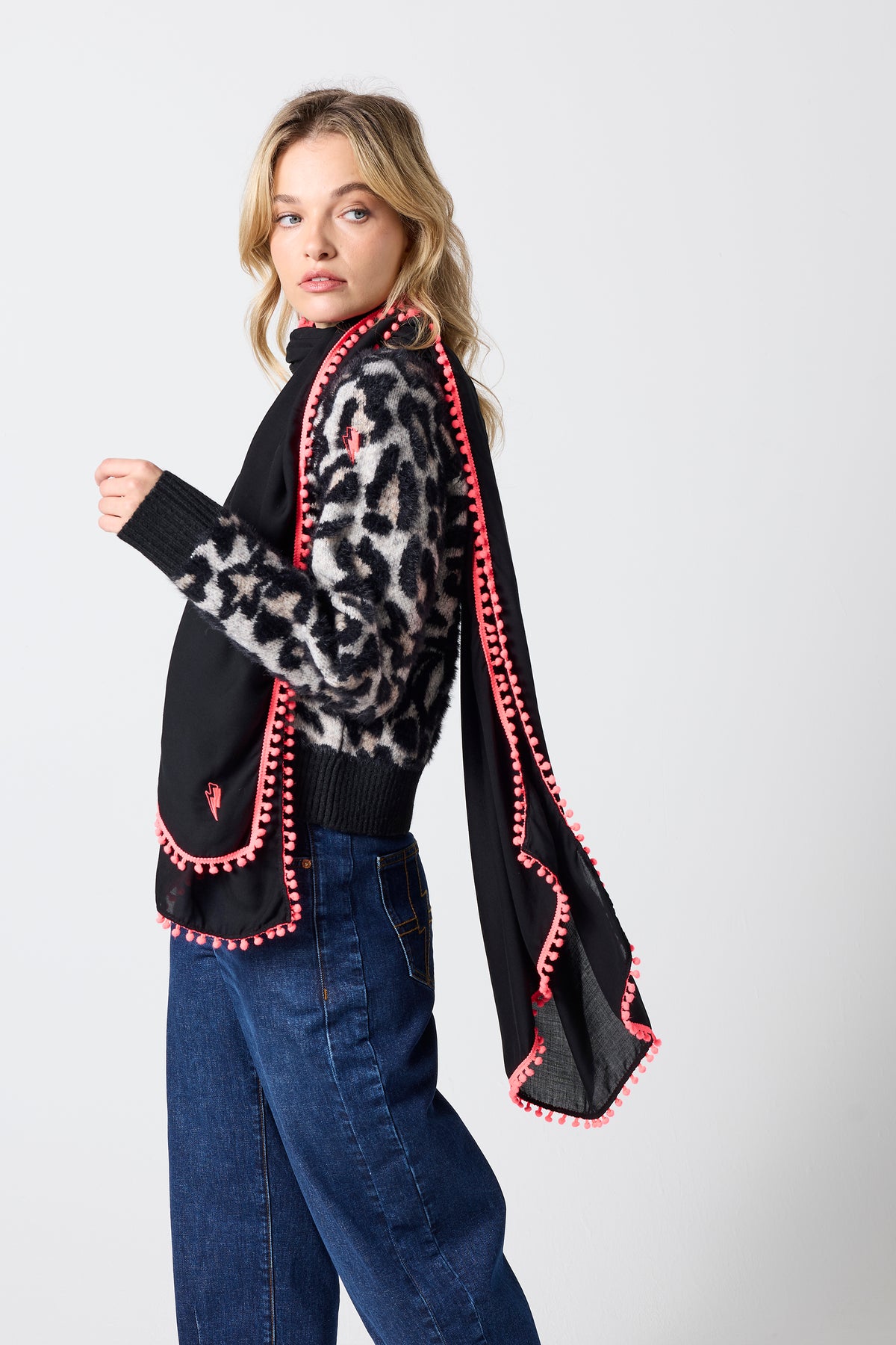 Scamp & Dude Black Charity Super Scarf | Model wearing a black super scarf with a neon coral trim. Paired with a neutral star leopard cardigan and dark blue barrel jeans.