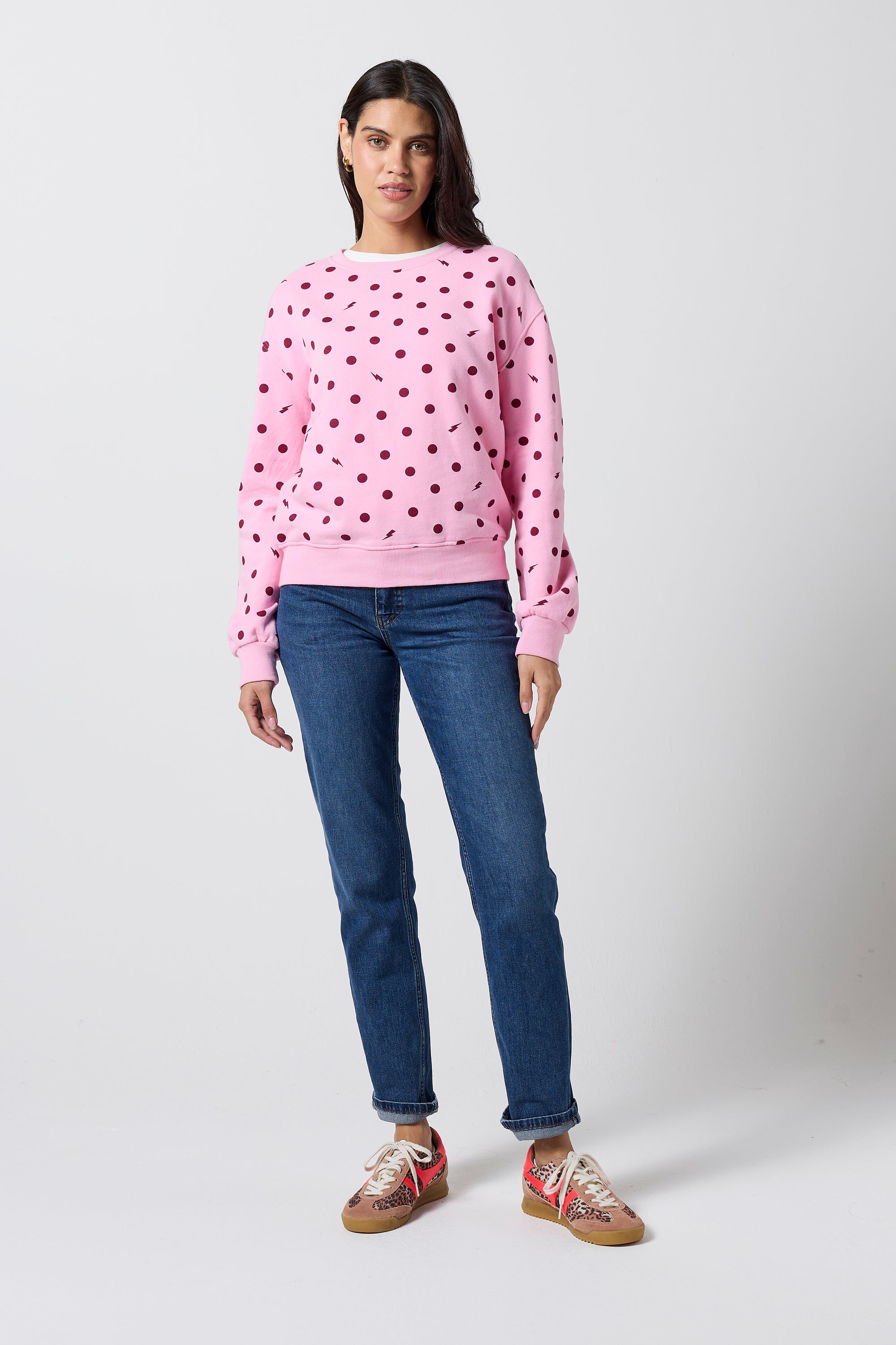 Scamp & Dude Pink Polka Dot Bolt Sweatshirt | Model wearing a pink polka dot sweatshirt with blue jeans and a pair of neutral cheetah print trainers.