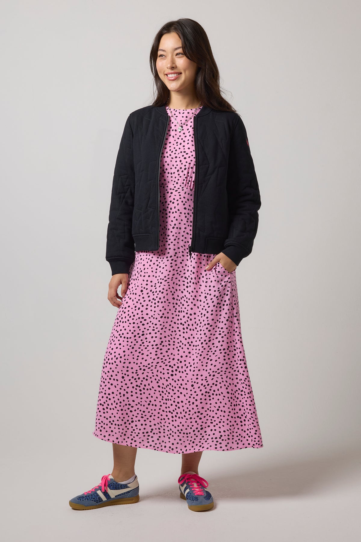 Scamp & Dude Black Lightning Bolt Fitted Quilted Bomber Jacket | Model wearing a pink midi dress with black polka dots, styled with a black quilted bomber jacket.